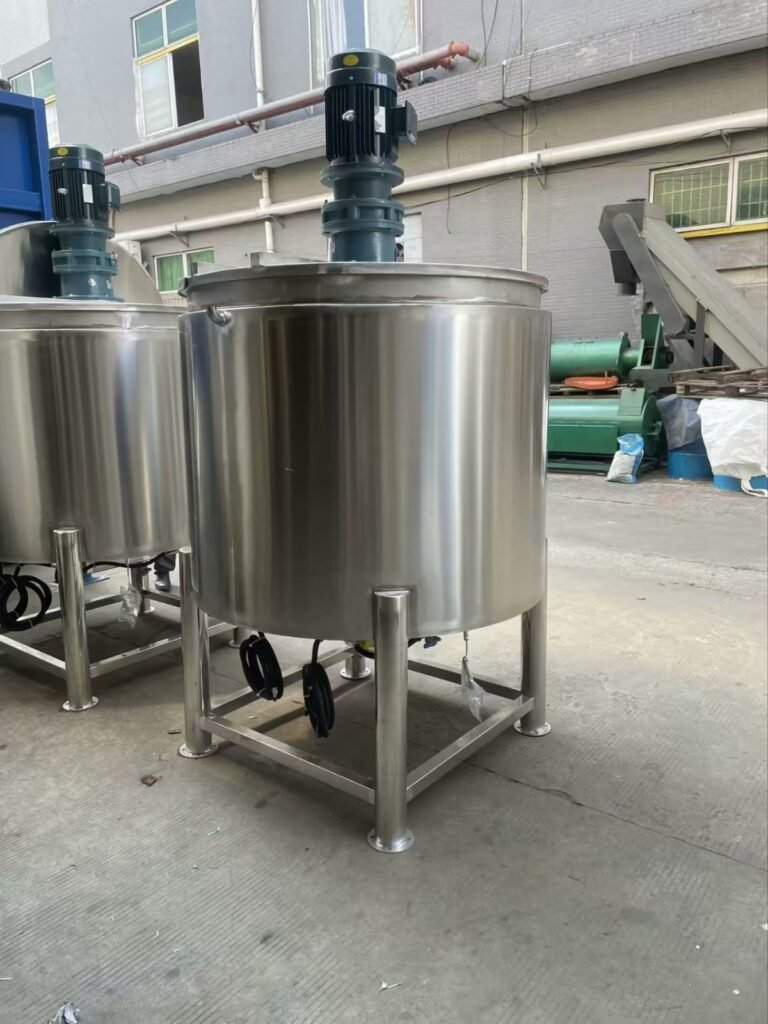 A large, industrial-grade stainless steel mixing tank with a top-mounted blue motor, situated on a metal platform with a small staircase outdoors.