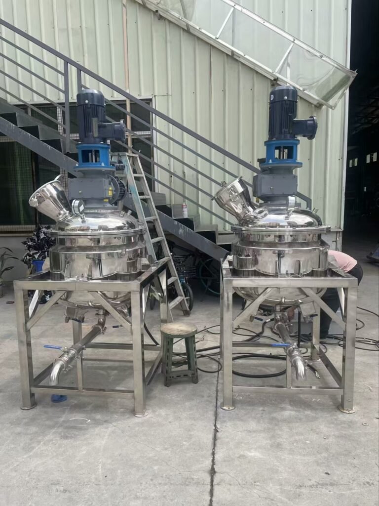 A wide shot of an outdoor industrial processing area featuring two large stainless steel tanks with blue top-mounted motors on a raised platform next to a building.