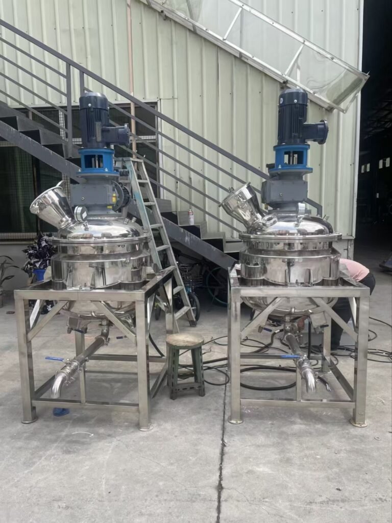 A pair of identical stainless steel industrial reactor vessels with top-mounted vertical agitator motors, positioned side-by-side on metal support frames in an outdoor facility.