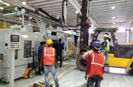 Filling machine service: Technicians installing packaging equipment with forklift support in a factory setting.
