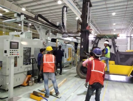 Filling machine service: Technicians installing packaging equipment with forklift support in a factory setting.