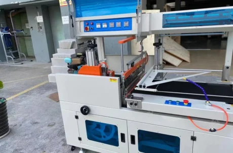 Shrink wrap packaging machine with conveyor belt and control panel, used for product protection.