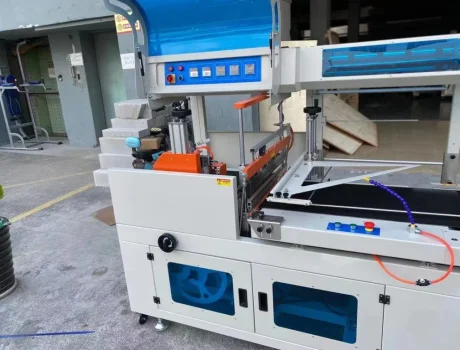 Shrink wrap packaging machine with conveyor belt and control panel, used for product protection.