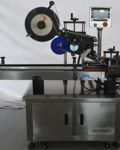 A stainless steel Top and Bottom Labeling Machine with a conveyor belt, control panel, and label roll, designed for applying labels to products in an industrial setting.