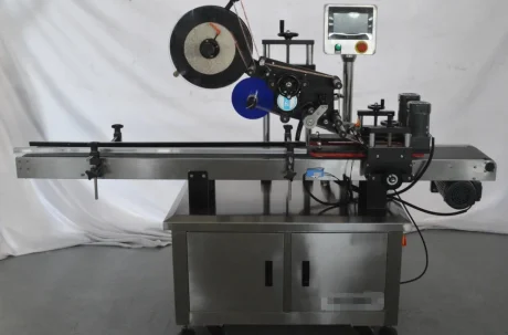 A stainless steel Top and Bottom Labeling Machine with a conveyor belt, control panel, and label roll, designed for applying labels to products in an industrial setting.