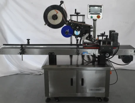 A stainless steel Top and Bottom Labeling Machine with a conveyor belt, control panel, and label roll, designed for applying labels to products in an industrial setting.