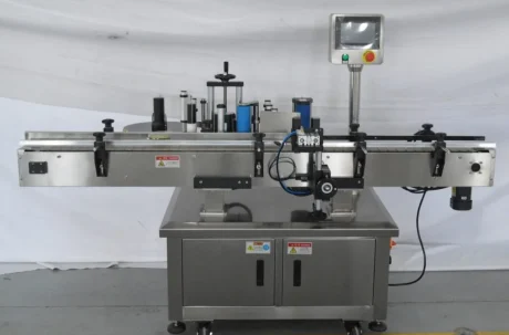 A stainless steel Round Bottle Labeling Machine with a conveyor belt, control panel, and rollers, designed for applying labels to bottles or containers in an industrial setting.