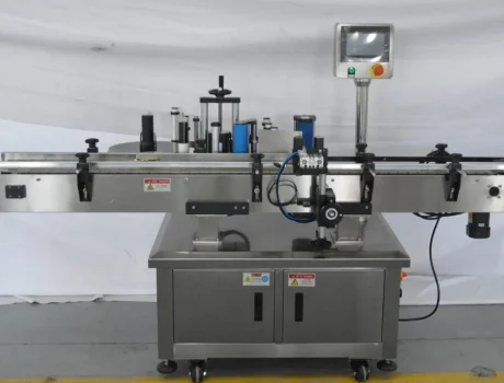 A stainless steel Round Bottle Labeling Machine with a conveyor belt, control panel, and rollers, designed for applying labels to bottles or containers in an industrial setting.