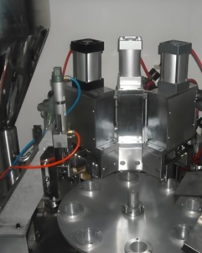 The machine applies the final seal to cosmetic tubes as they move along the conveyor.