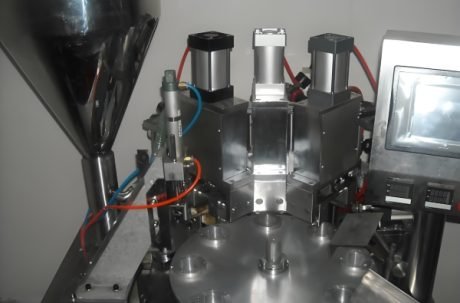 The machine applies the final seal to cosmetic tubes as they move along the conveyor.