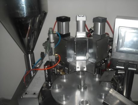 The machine applies the final seal to cosmetic tubes as they move along the conveyor.