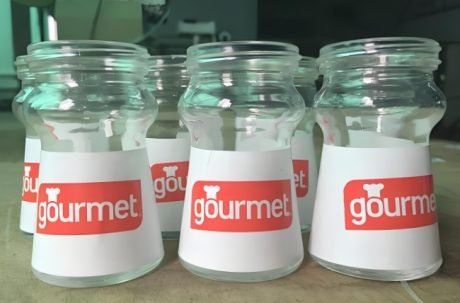 Glass containers labeled "gourmet" using a labeling machine.