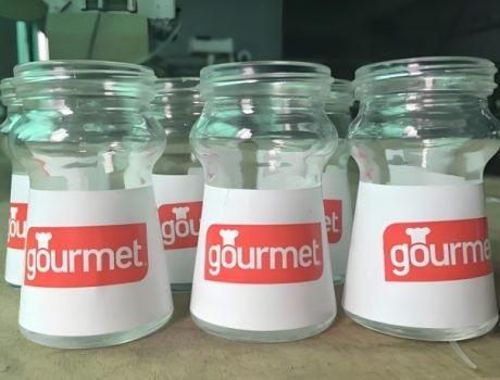 Glass containers labeled "gourmet" using a labeling machine.